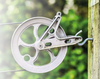 Ben-Mor clothesline pulley wheel mounted on wooden post — close up of aluminum pulley with steel cable running through it, green foliage background